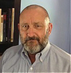 Headshot of a man with a beard, wearing a light blue shirt, in front of a bookshelf. Headshot of a man with a beard, wearing a light blue shirt, in front of a bookshelf.