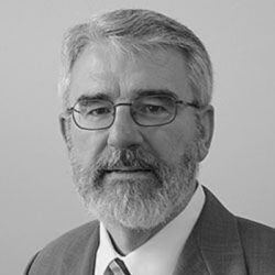 Headshot of a man with glasses and a beard, wearing a suit.