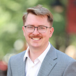 Smiling man in a gray suit with glasses outdoors